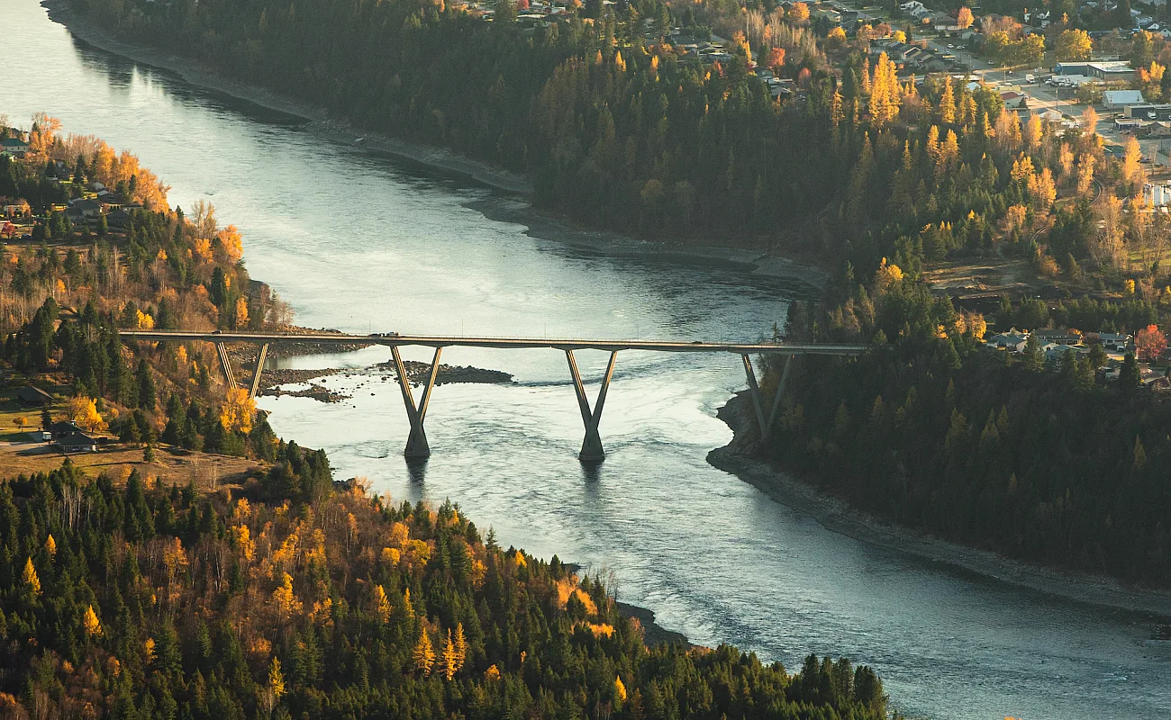 Mit Blick auf einen gewundenen Fluss, der von einer Brücke überquert wird, umgeben von dichtem Wald und Herbstfarben.