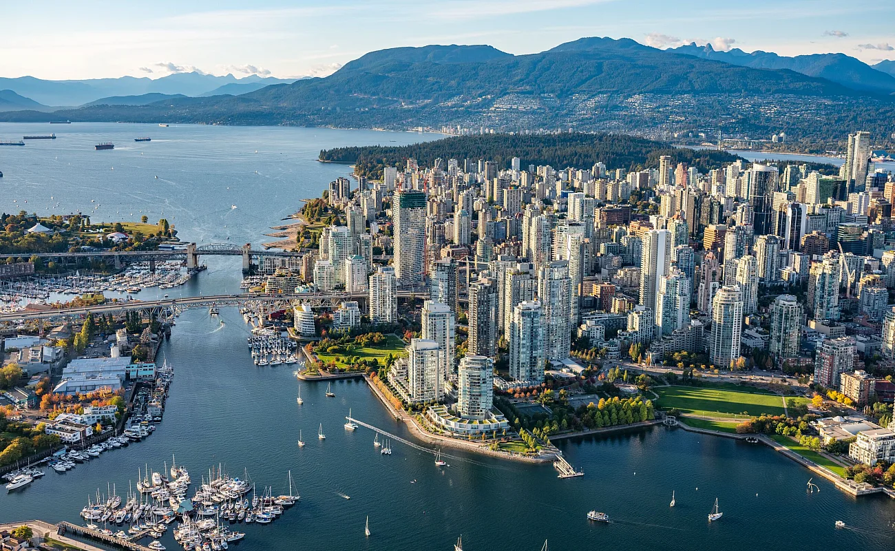 Aerial photo of downtown Vancouver with boats dotting False Creek in the foreground backed by the towers of the downtown core, and English Bay and the North Shore Mountains beyond