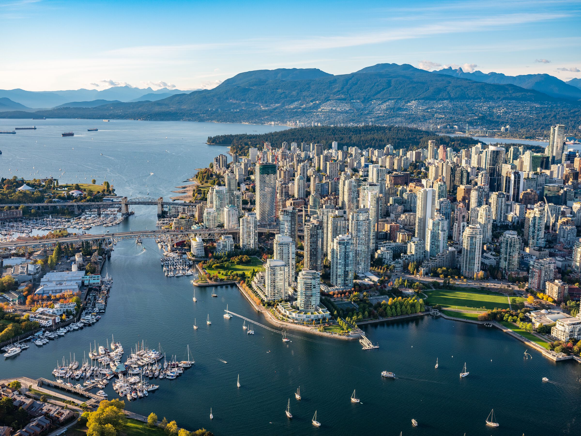 Aerial photo of downtown Vancouver with boats dotting False Creek in the foreground backed by the towers of the downtown core, and English Bay and the North Shore Mountains beyond