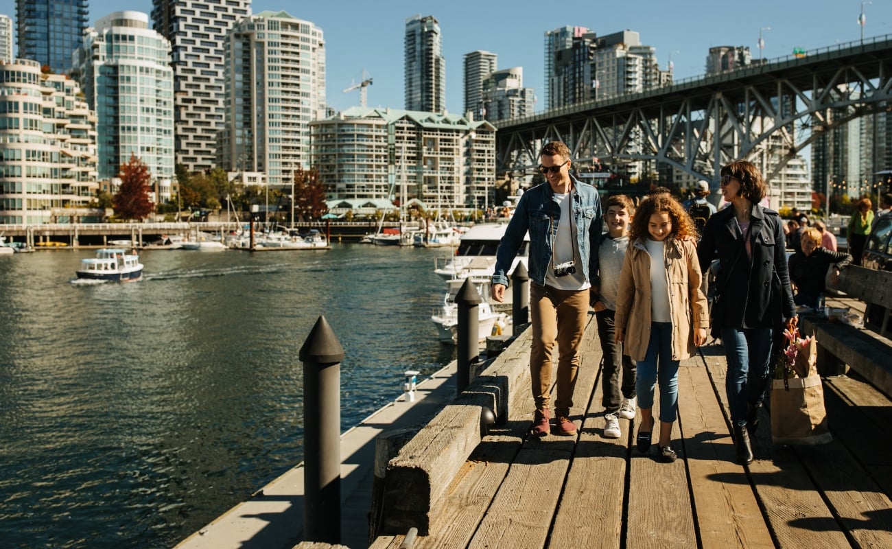 Family walking outside at Granville Island with the city in the background.