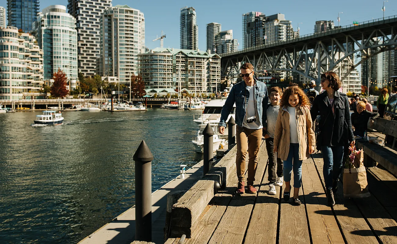 Familie beim Spaziergang auf Granville Island mit der Stadt im Hintergrund.