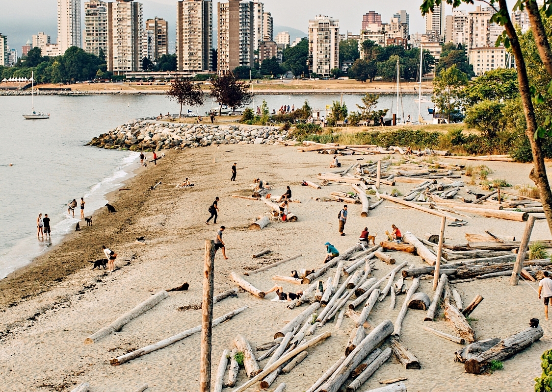 Sandy beach strewn with logs, the towers of downtown Vancouver in the background.