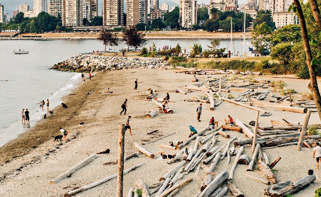 Sandy beach strewn with logs, the towers of downtown Vancouver in the background.