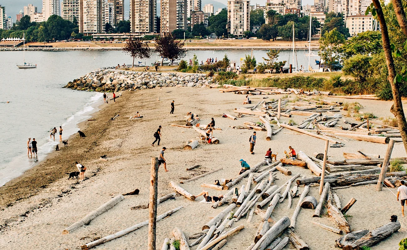 Ein mit Baumstämmen übersäter Sandstrand, im Hintergrund die Türme der Innenstadt von Vancouver.