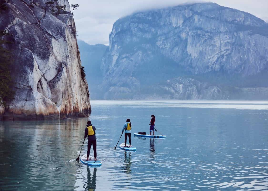 Drei Paddleboarder*innen umgeben von massiven Felsen.