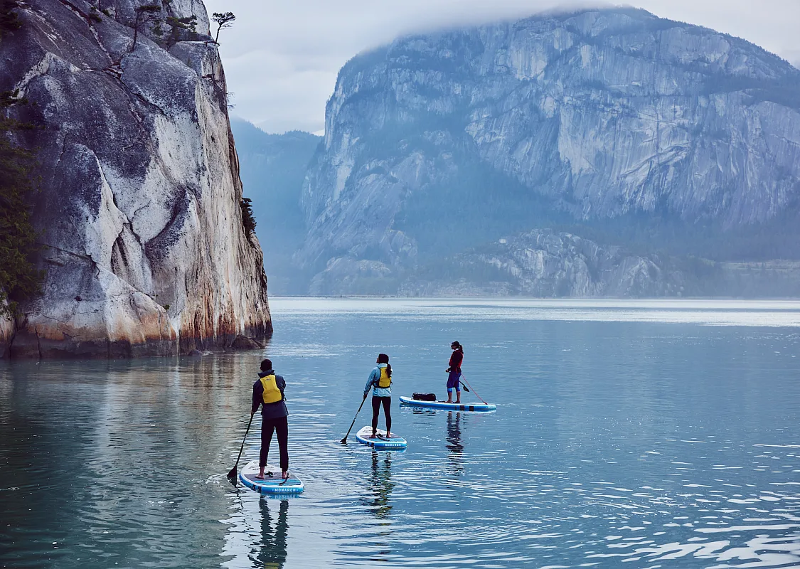 Drei Paddleboarder*innen umgeben von massiven Felsen.