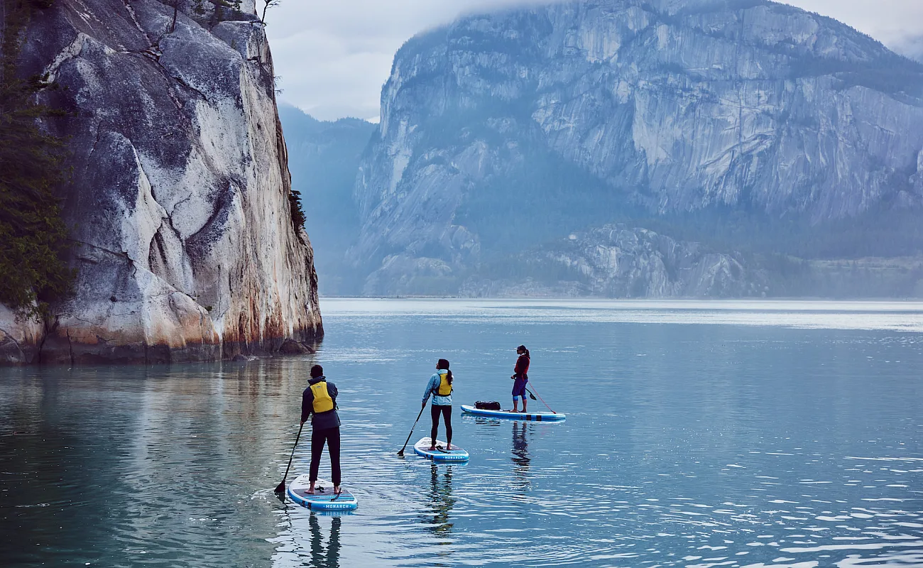 Drei Paddleboarder*innen umgeben von massiven Felsen.