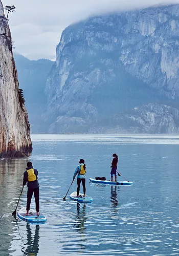 Drei Paddleboarder*innen umgeben von massiven Felsen.