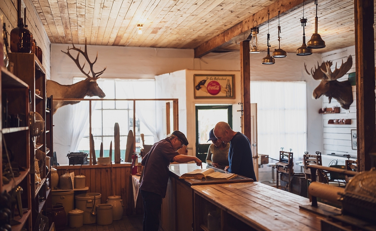 People chatting over the counter in a historic building at Walter Wright Pioneer Village in Dawson Creek, BC.