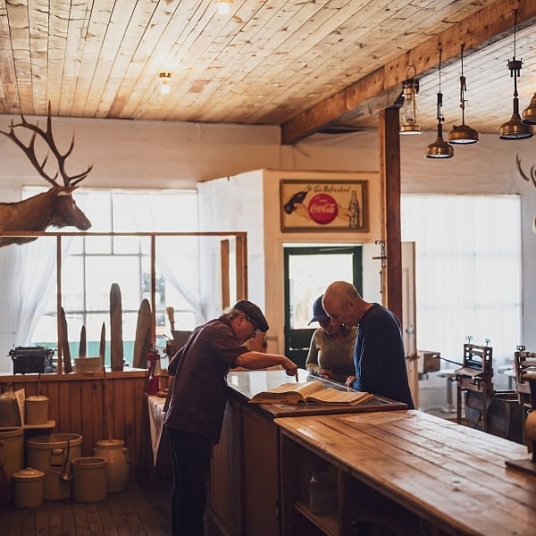 People chatting over the counter in a historic building at Walter Wright Pioneer Village in Dawson Creek, BC.