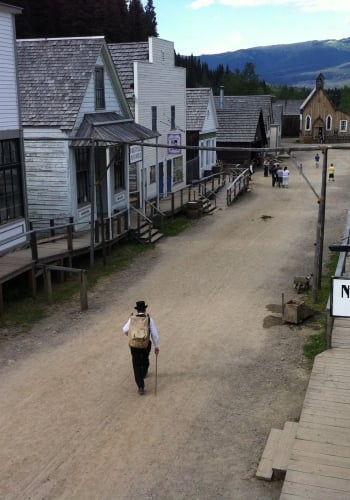 A person in period costume walks down a street of heritage buildings at Barkerville Historic Town.
