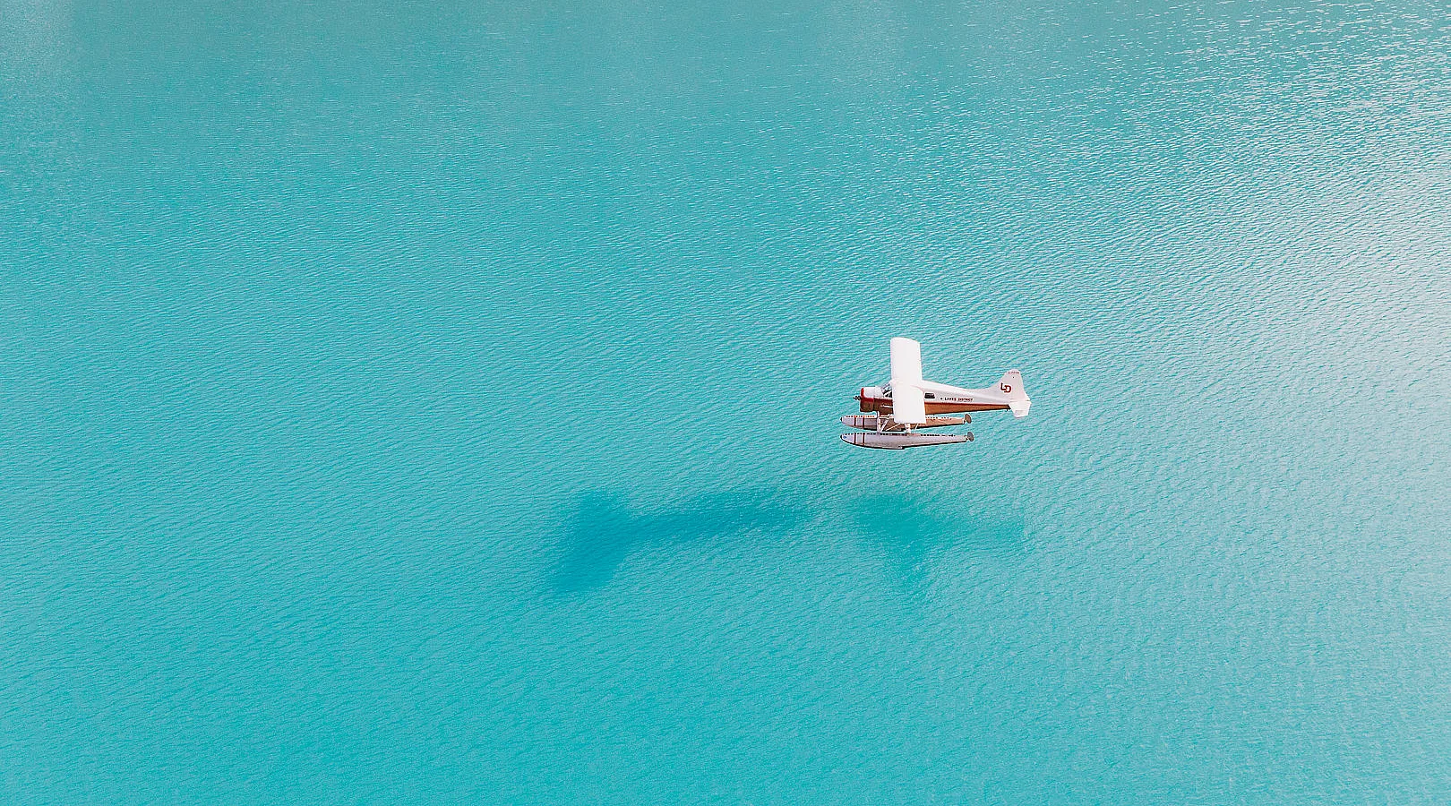 Dieses Standbild ist ein Platzhalter für ein Video. Ein Wasserflugzeug über einem gletscherblauen See. Das Flugzeug hat weiße Flügel und einen roten Rumpf.