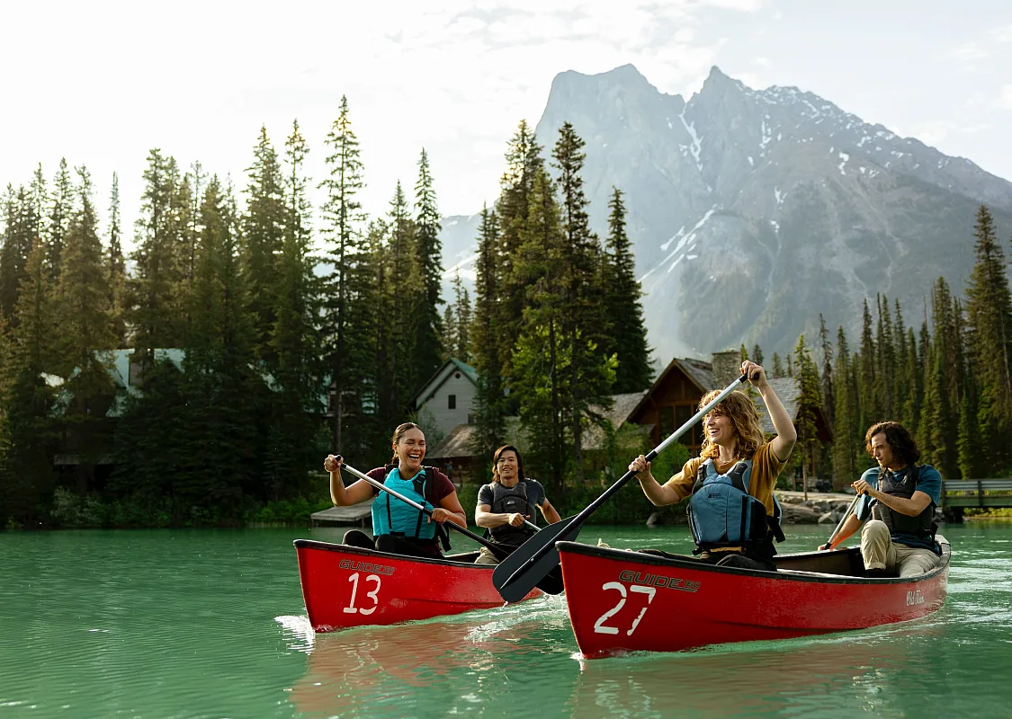 Cuatro amigos en canoa sobre las aguas turquesas del lago Emerald en el Parque Nacional Yoho en las Montañas Rocosas canadienses, con Emerald Lake Lodge al fondo.