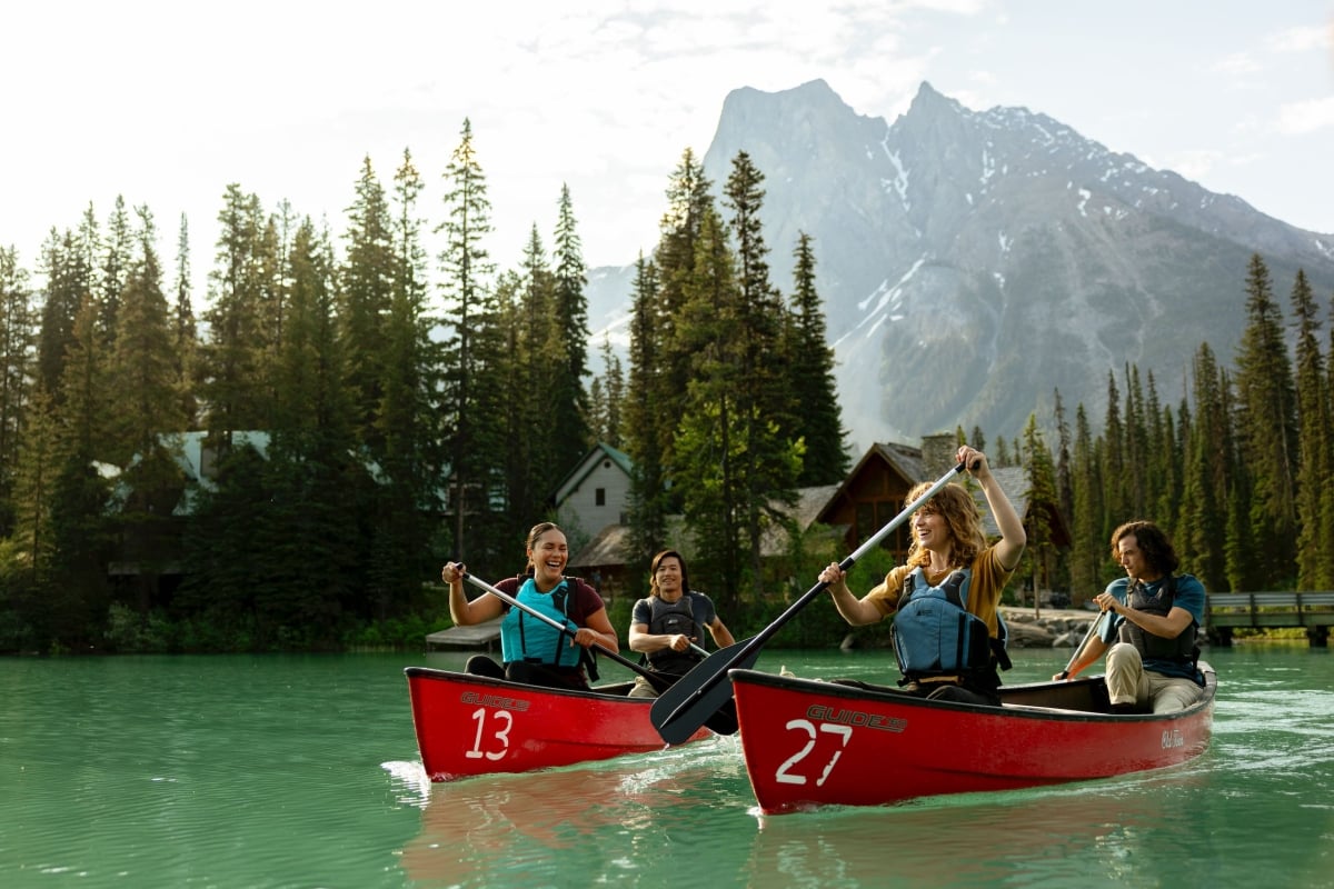 Vier Freunde paddeln auf dem türkisfarbenen Wasser des Emerald Lake im Yoho National Park in den kanadischen Rockies, mit der Emerald Lake Lodge im Hintergrund.