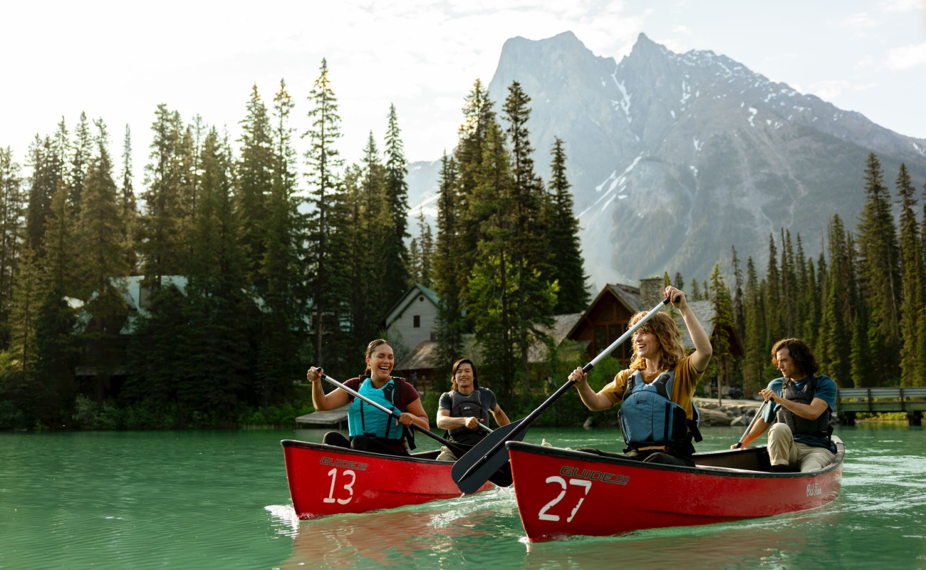 Four friends canoeing on the turquoise waters of Emerald Lake in Yoho National Park in the Canadian Rockies, with Emerald Lake Lodge in the background.