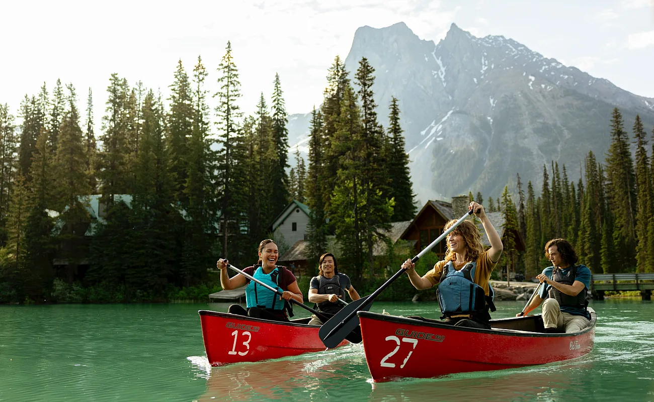 Four friends canoeing on the turquoise waters of Emerald Lake in Yoho National Park in the Canadian Rockies, with Emerald Lake Lodge in the background.