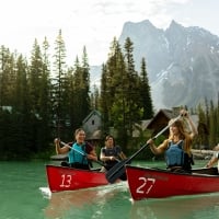 Four friends canoeing on the turquoise waters of Emerald Lake in Yoho National Park in the Canadian Rockies, with Emerald Lake Lodge in the background.