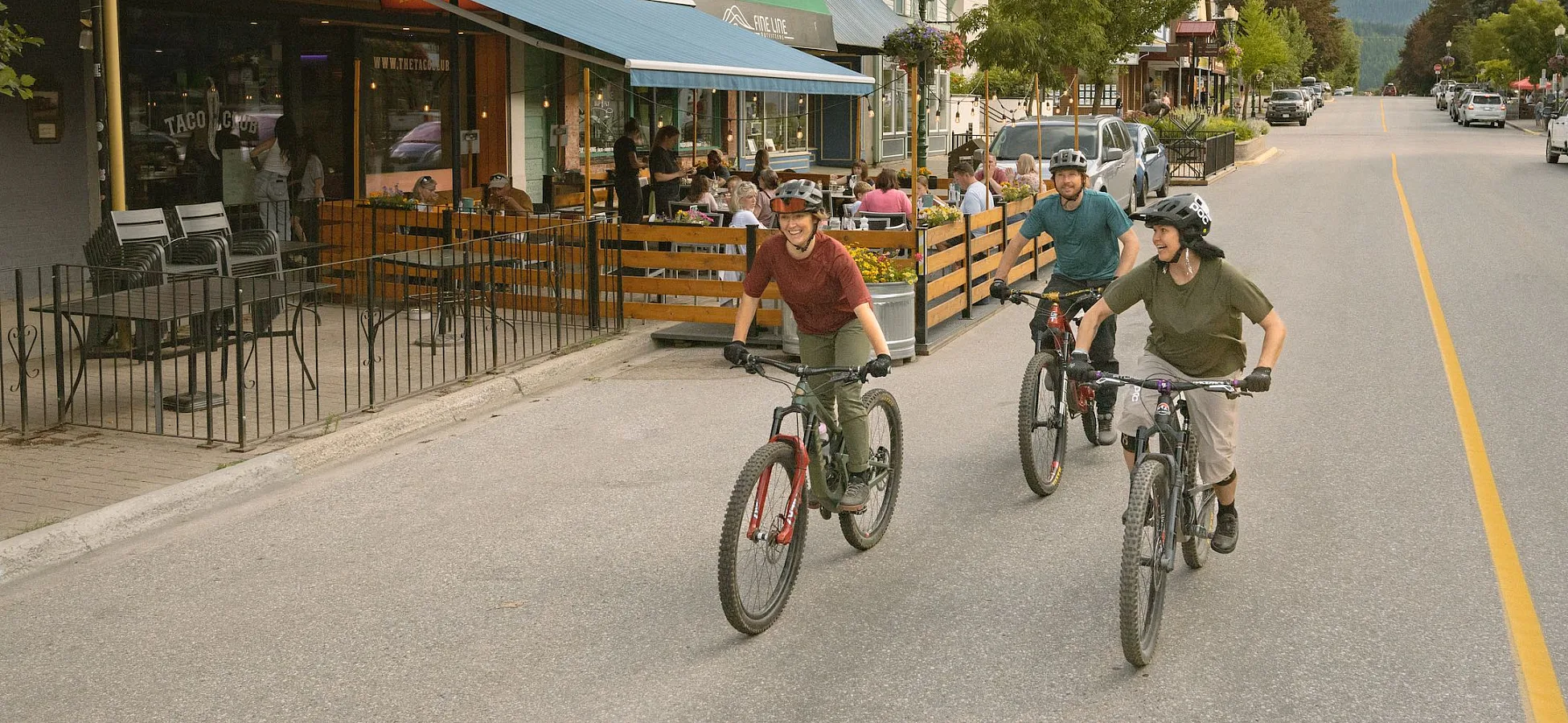 Three friends enjoy a bike ride in downtown Revelstoke as locals grab a bite to eat on The Taco Club patio.