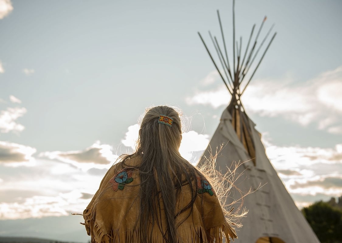Ktunaxa elder in regalia next to a teepee at St Eugene Golf Resort