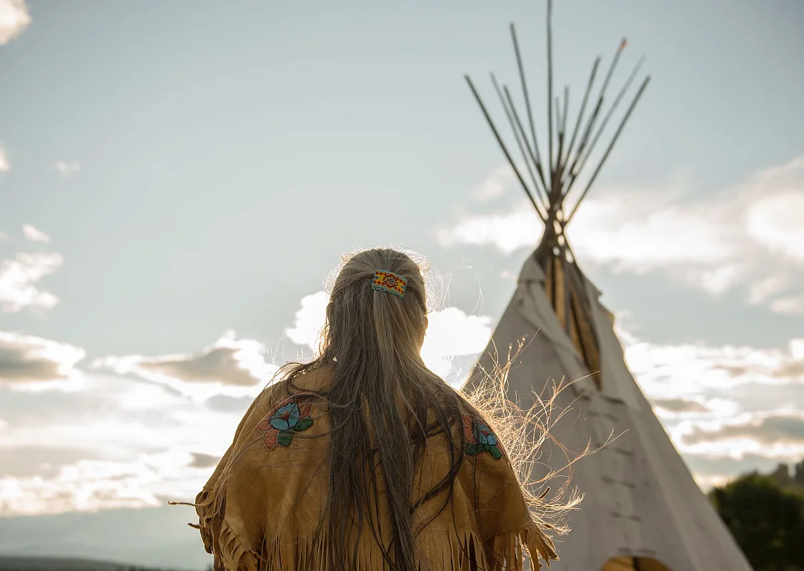 Ktunaxa elder in regalia next to a teepee at St Eugene Golf Resort