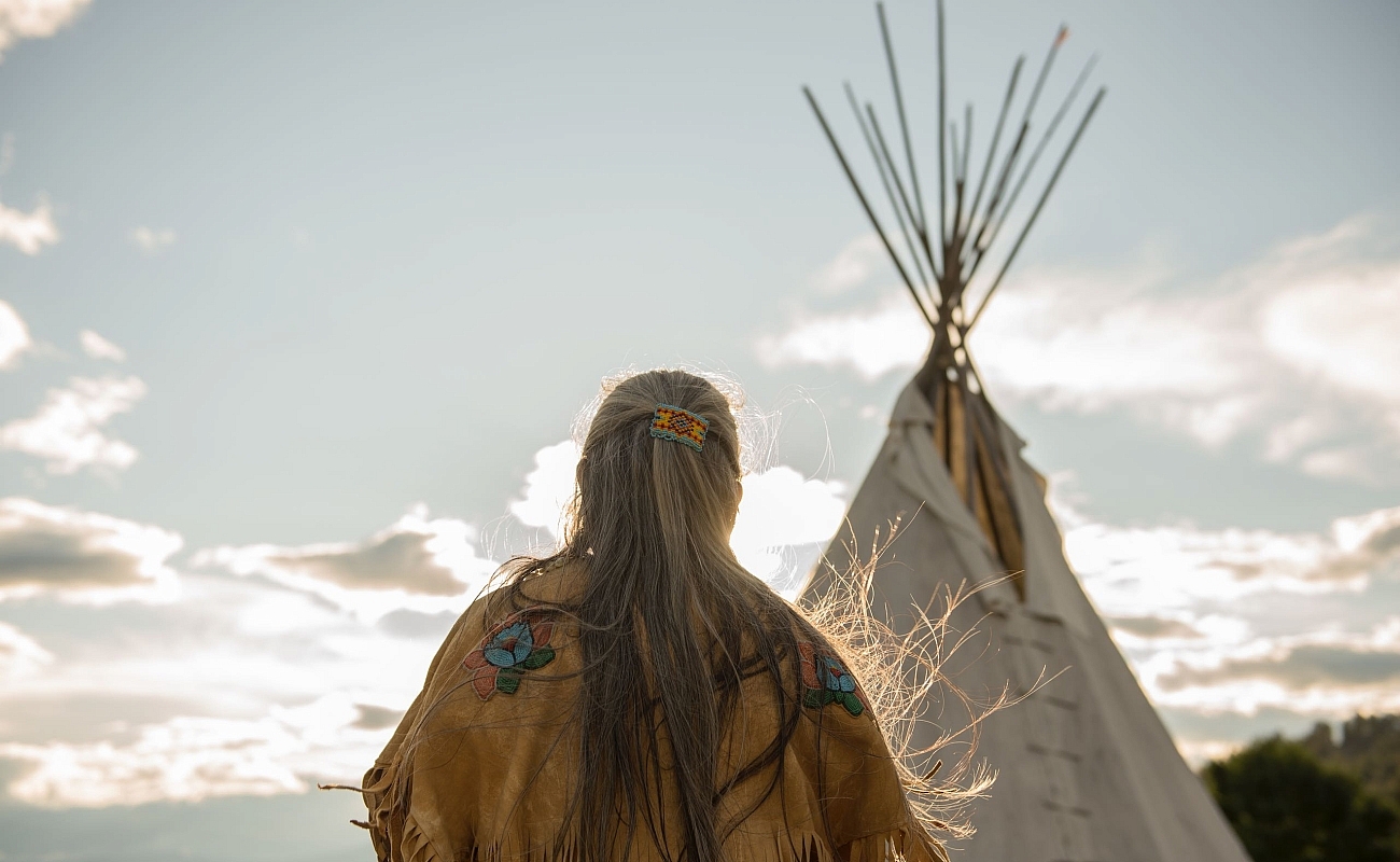 Ktunaxa-Älteste*r in traditioneller Kleidung neben einem Tipi im St Eugene Golf Resort