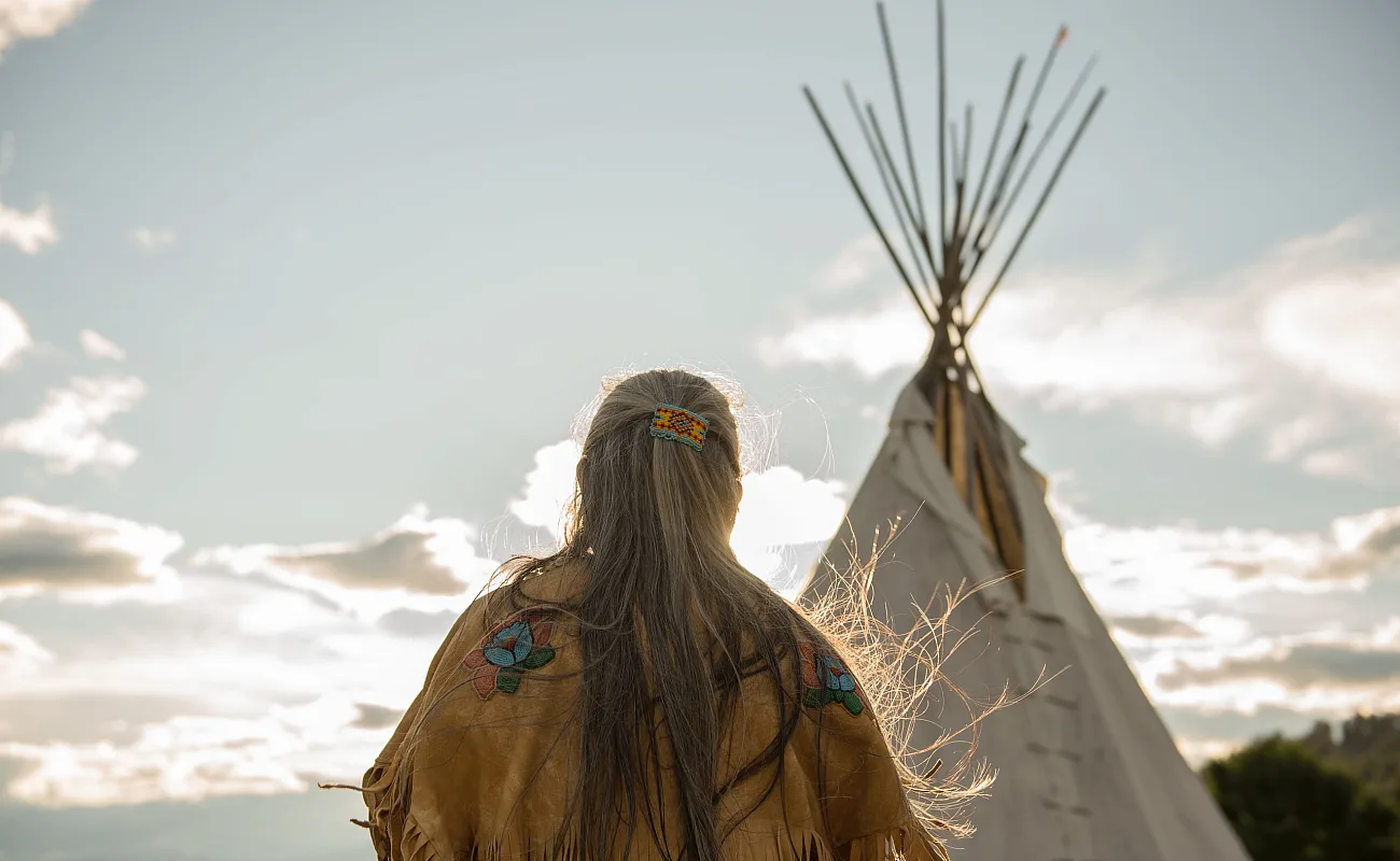 Ktunaxa-Älteste*r in traditioneller Kleidung neben einem Tipi im St Eugene Golf Resort