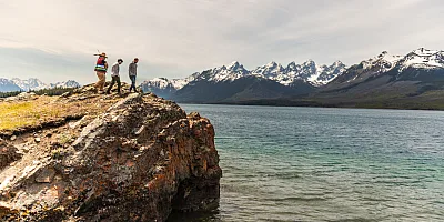 A father and son climbing a rock with their Indigenous guide while on a tour at Chilko Lake in Ts’ilʔos Provincial Park, with the scenic mountains in the background.