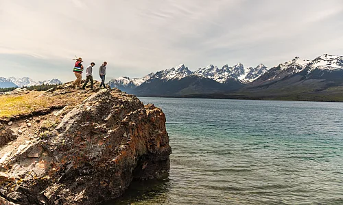 A father and son climbing a rock with their Indigenous guide while on a tour at Chilko Lake in Ts’ilʔos Provincial Park, with the scenic mountains in the background.