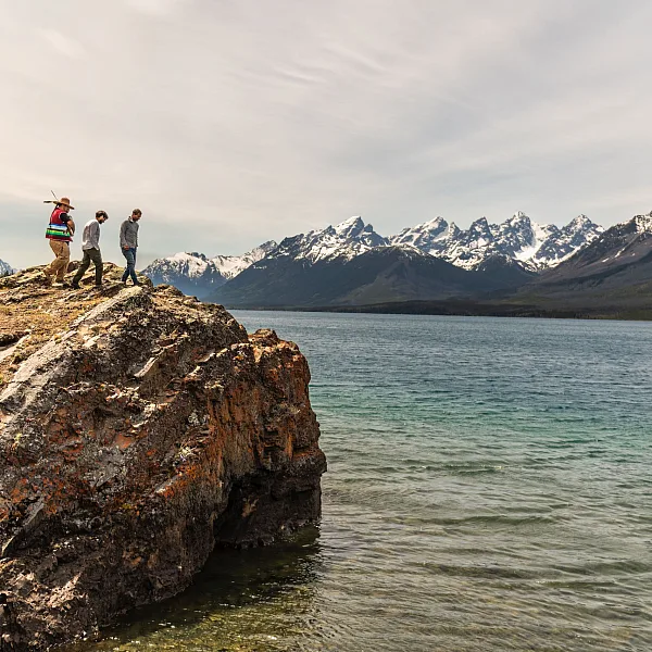 Un padre y un hijo escalando una roca con su guía indígena durante un recorrido por el lago Chilko en el Parque Provincial Ts’ilʔos, con las pintorescas montañas de fondo.