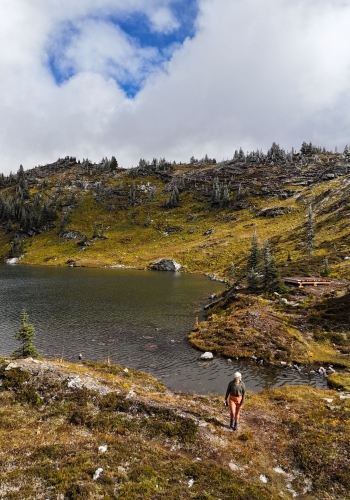 A drone shot of a person walking on a trail on Trophy Mountain with Sheila Lake in the background.