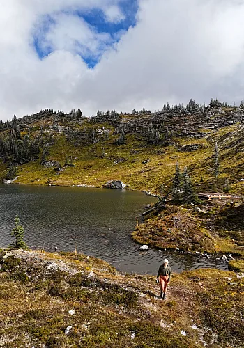 Una toma con dron de una persona caminando por un sendero en Trophy Mountain con Sheila Lake al fondo.