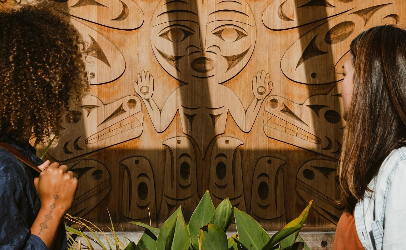 Two people taking in an Indigenous carving on the exterior wall at the Gibsons Public Art Gallery.