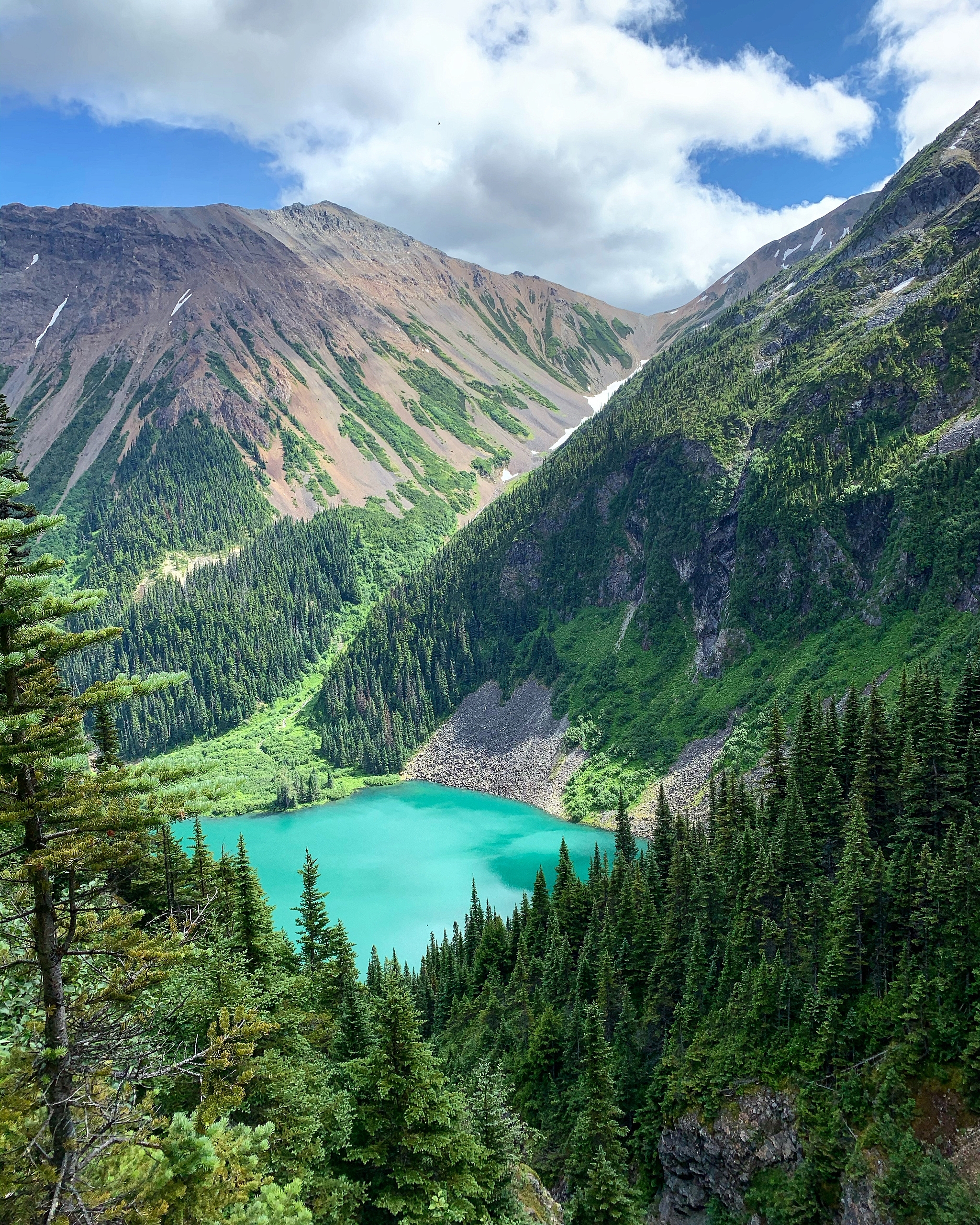 A colourful mountain scene centring around a vibrant blue lake that is surrounded by orange mineral mountains and flanked by by lush green forest.