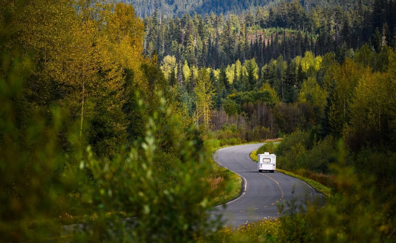 An RV drives down a winding highway surrounded by great wilderness.
