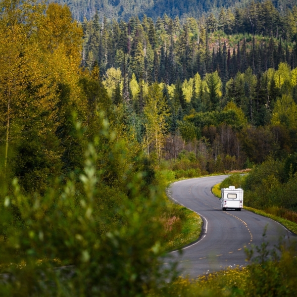An RV drives down a winding highway surrounded by great wilderness.