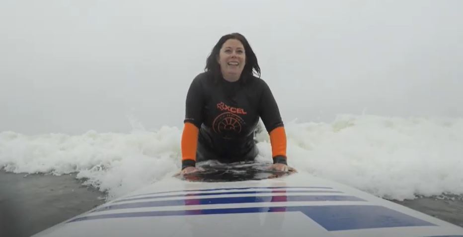 A woman on a surfboard in the wake near shore. She is pushing up on the board.