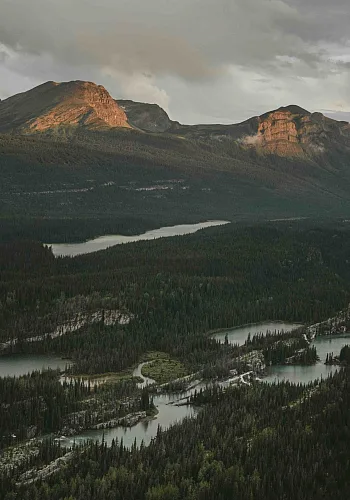 A mountain range at sunset in the Northern Rockies. A river system flows in the valley below.