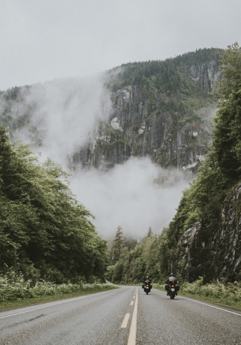 Two motorcycles ride down Route 16 between lush green forest.
