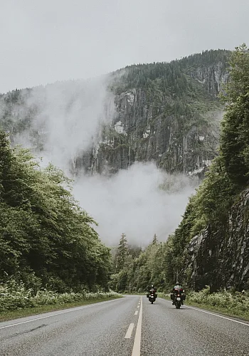 Zwei Motorräder fahren auf der Route 16 zwischen üppig grünem Wald entlang.
