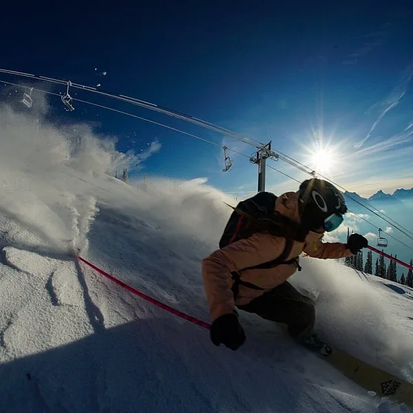 A close up of a skier on a deep turn with the chair lift behind them
