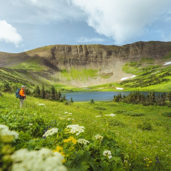A hiker in the foreground walks past a lake with a mountain ridge behind.