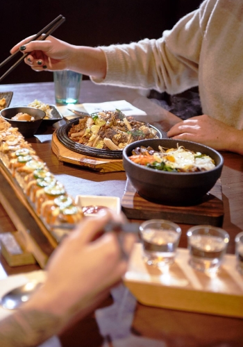 A closeup of two people's hands as they eat a meal at Sooda Korean BBQ restaurant at Brentwood Town Centre in Burnaby.