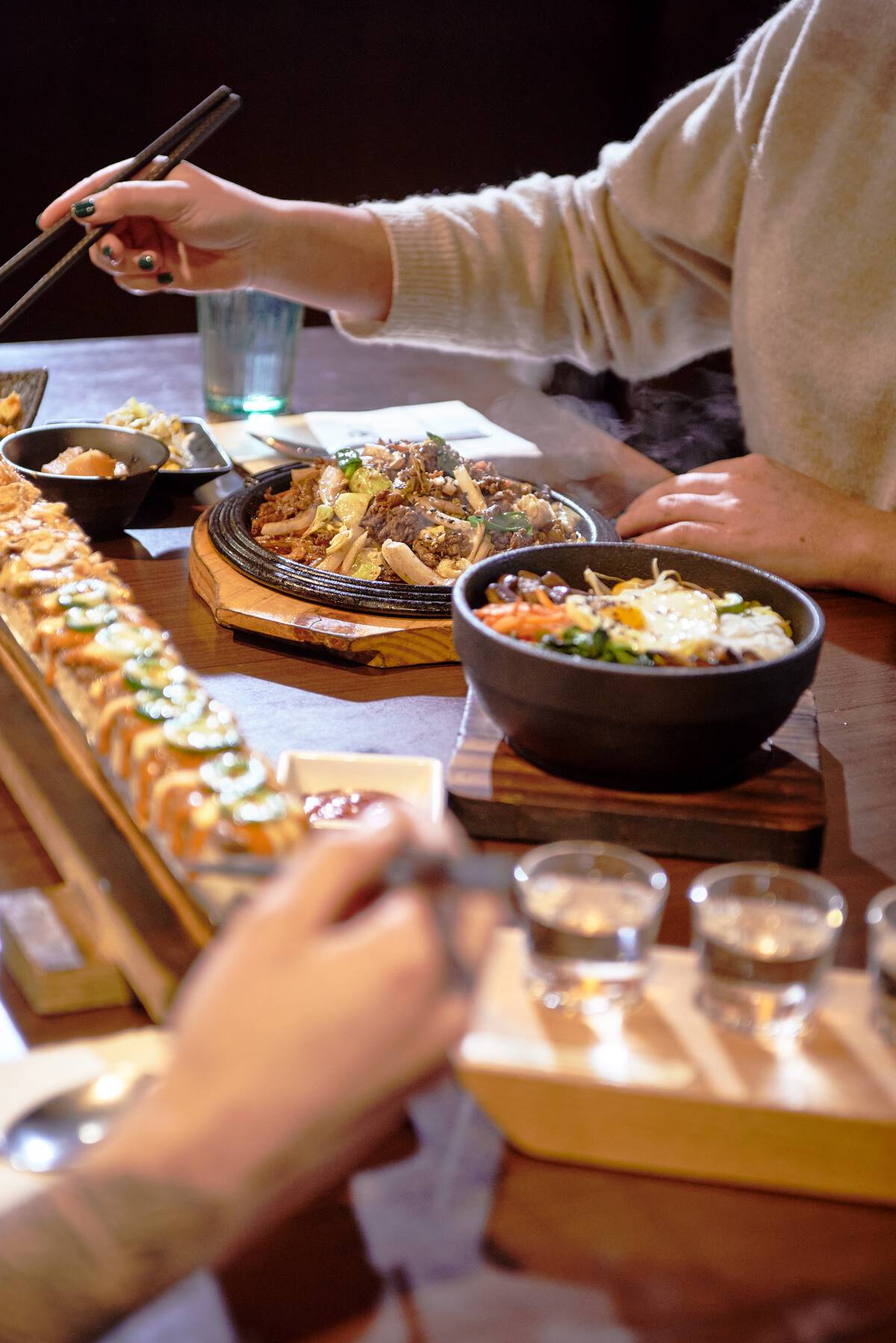 A closeup of two people's hands as they eat a meal at Sooda Korean BBQ restaurant at Brentwood Town Centre in Burnaby.