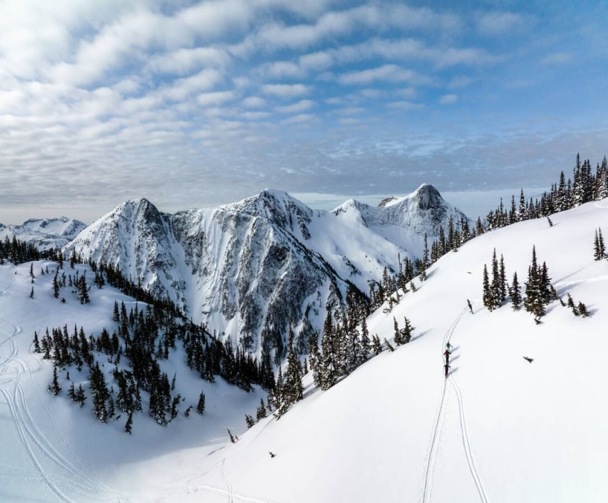 Three people walking up the side of a snow-covered mountain with their ski gear