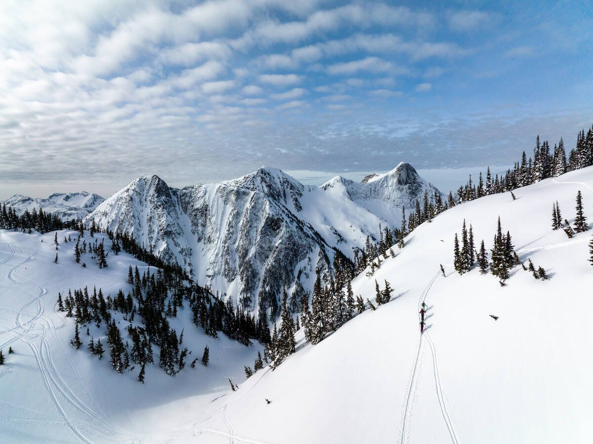 Three people walking up the side of a snow-covered mountain with their ski gear