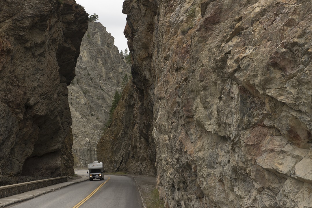 An RV driving through Sinclari Canyon with tall rock walls on either side of the road.