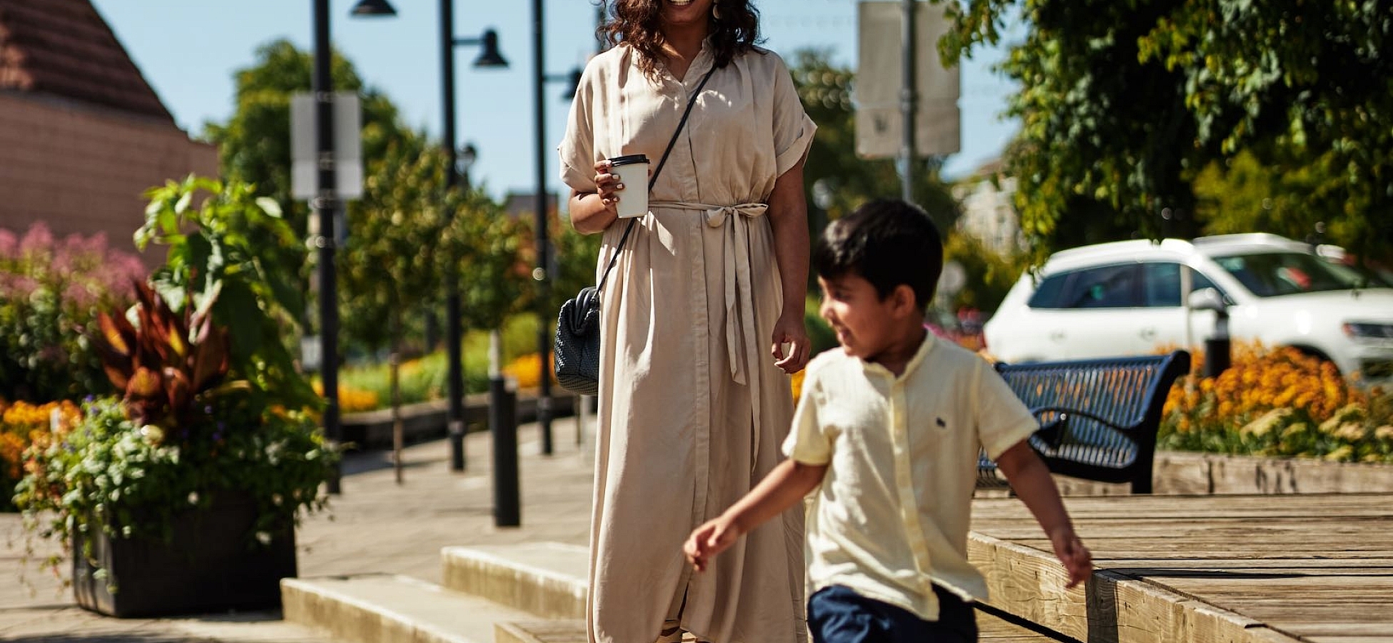 A person and a child are walking along a wooden boardwalk in the city.