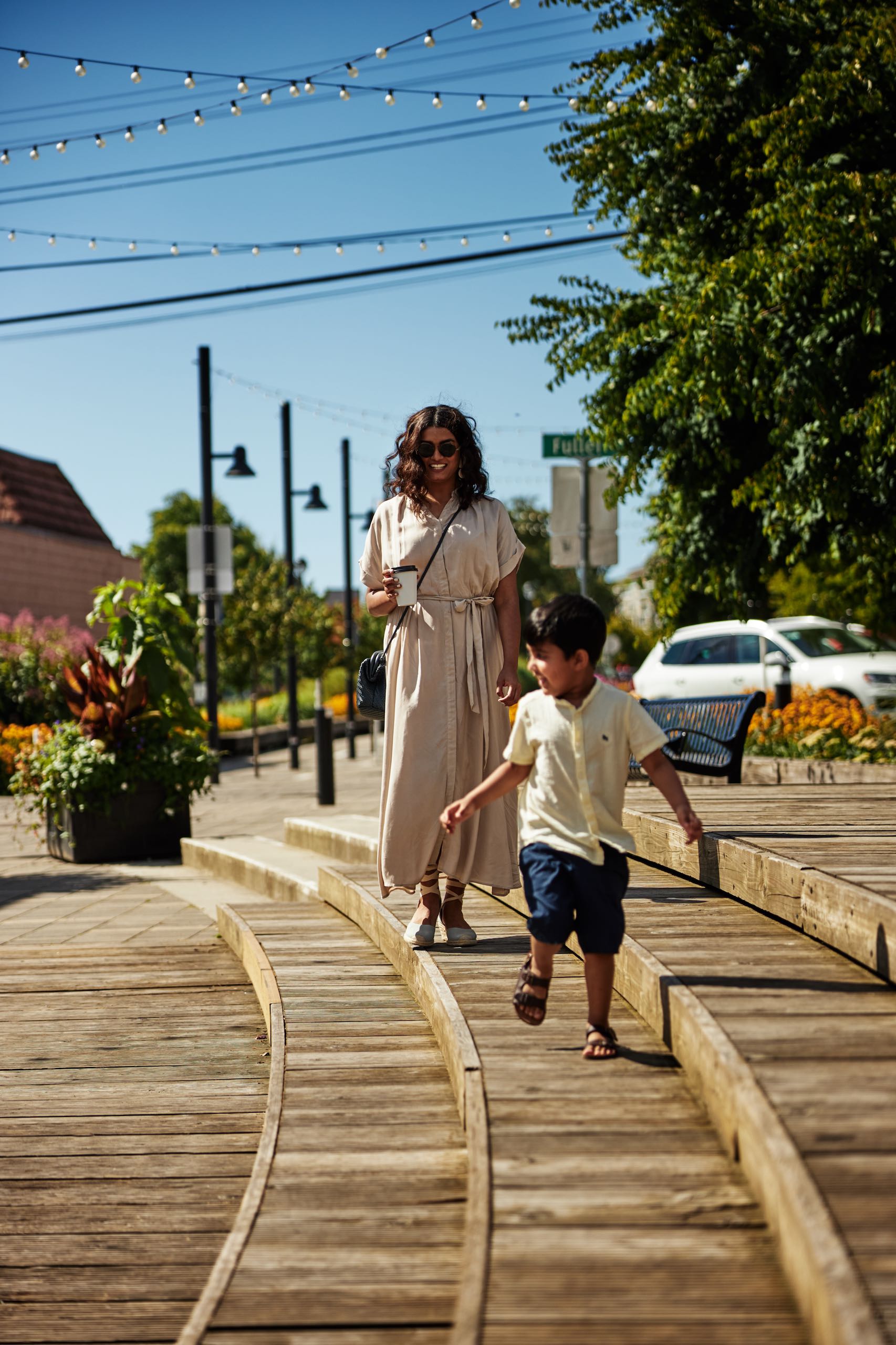 A person and a child are walking along a wooden boardwalk in the city.