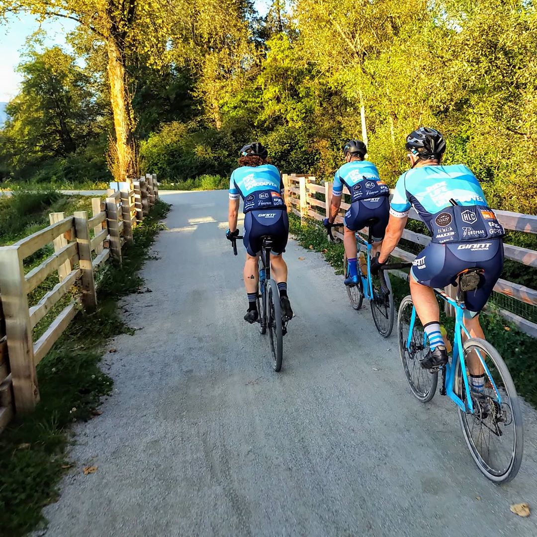 Three cyclists on turquoise bikes riding along a curved gravel path lined by wooden fences on each side with trees ahead of the path.