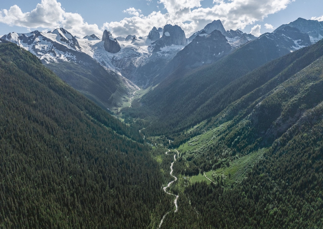 An aerial view of the trees, mountain spires, and glacial turquoise waters in the Bugaboos mountain range, captured during a heli-hiking trip with CMH Bugaboos.